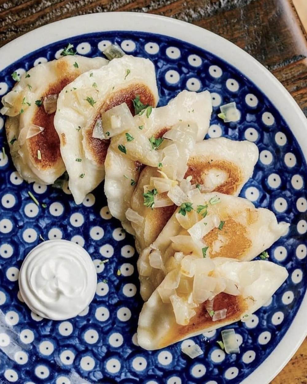 Pan-fried handmade pierogi with sautéed onions and sour cream on blue Bolesławiec Polish pottery